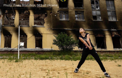 A girl plays volleyball against the background of a destroyed school in Kharkiv