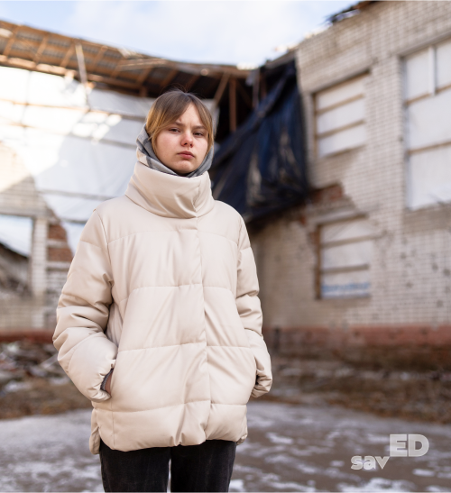 A girl in front of a destroyed school in the village of Chervona Dolyna